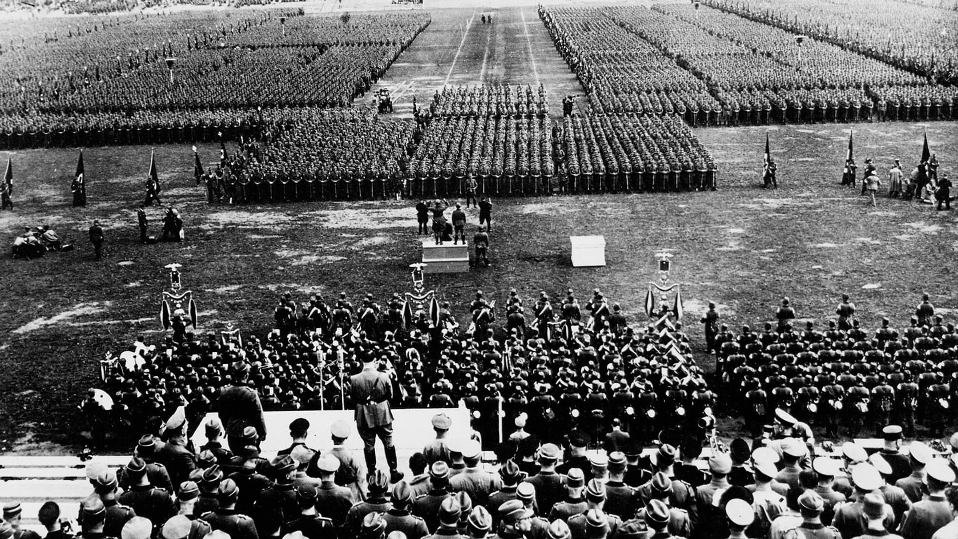 Hitler seen from behind on a stage facing tens of thousands of men lined up on the Zeppelin Field in Nuremberg in 1934