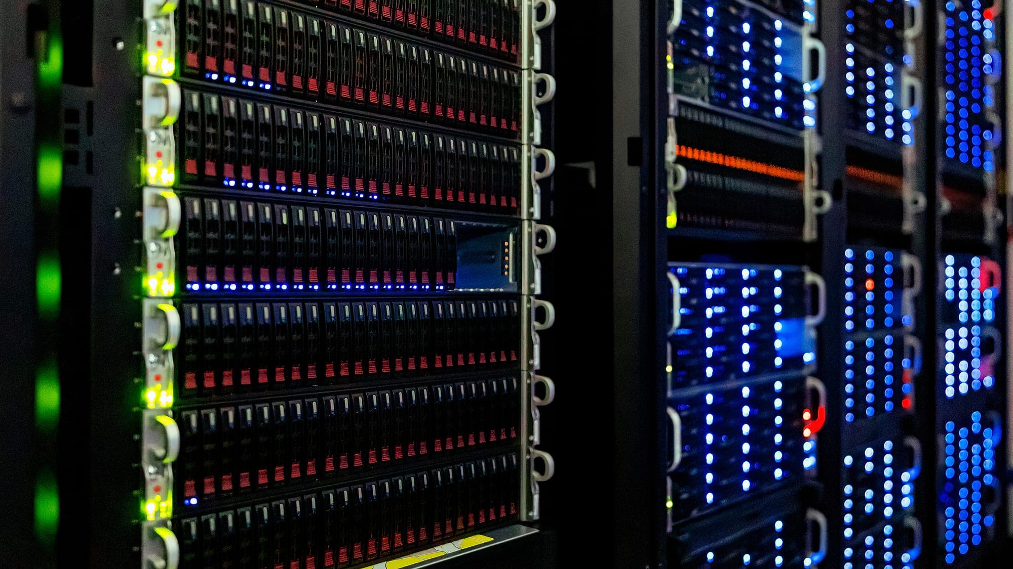 Server racks in a computer room, with the blue, red and green lights of the drives switched on