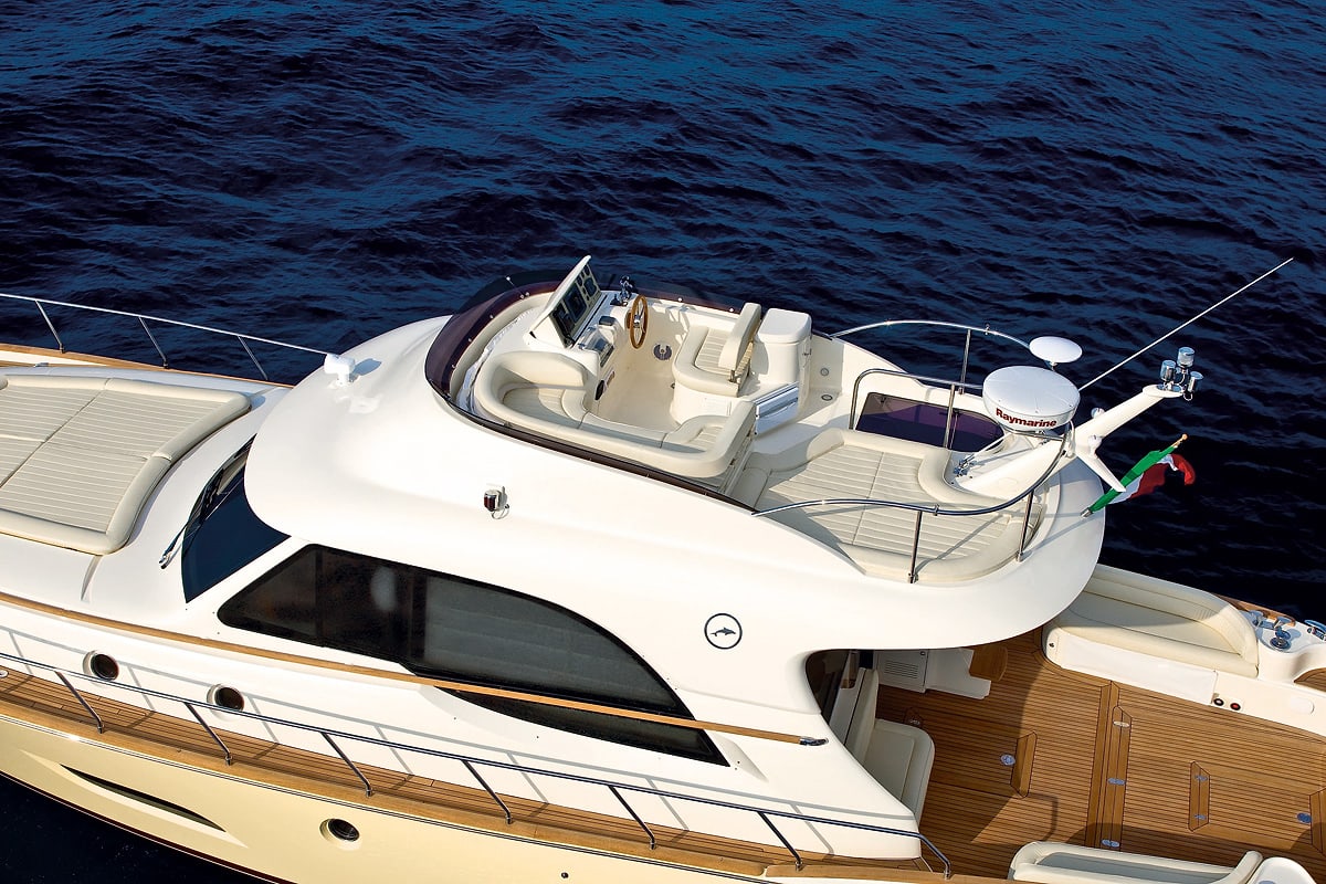 Uno yacht Mochi Craft bianco visto dall'alto sul mare blu scuro, con il posto di guida scoperto sul tetto, il prendisole a prua e il pozzetto in teak a poppa