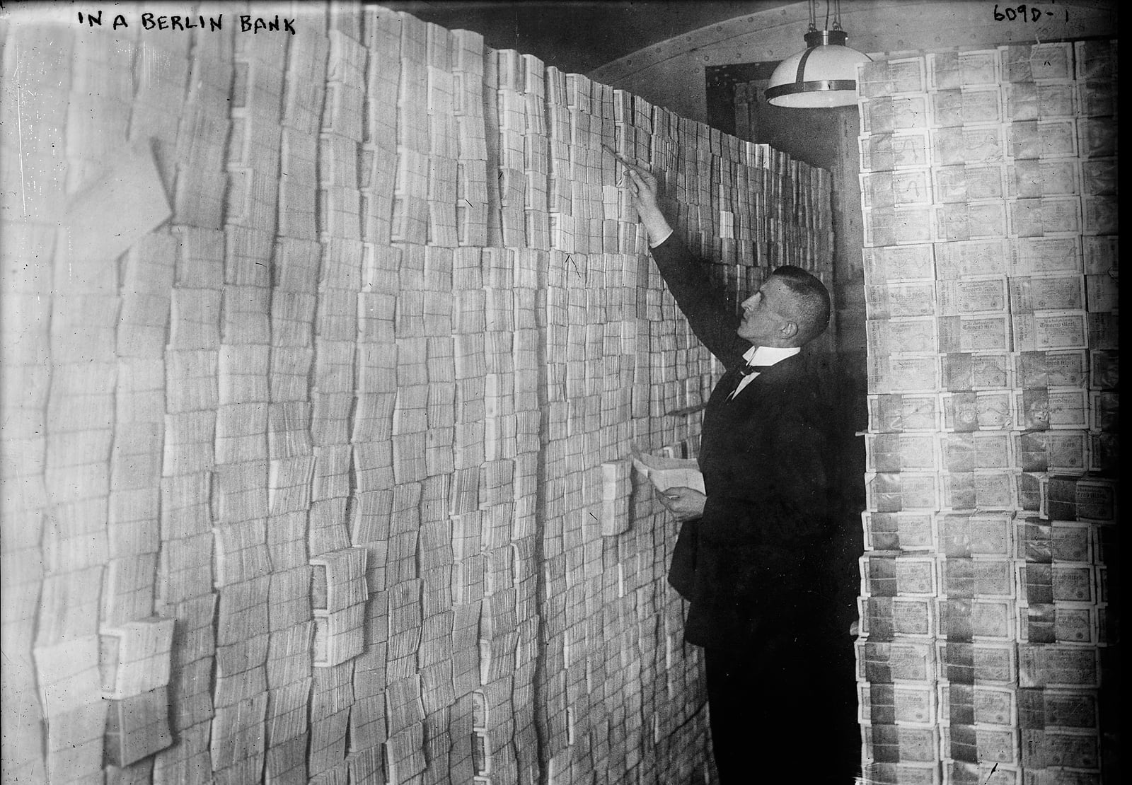 A clerk in front of a wall of banknote bundles stacked to the ceiling in a Berlin bank in 1923