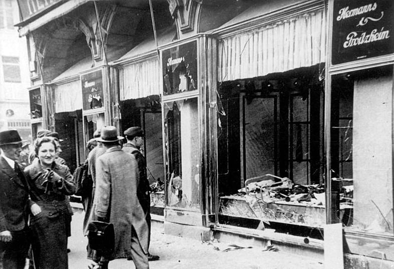 Passers-by in front of the smashed windows of a Jewish-owned shop in Magdeburg after Kristallnacht