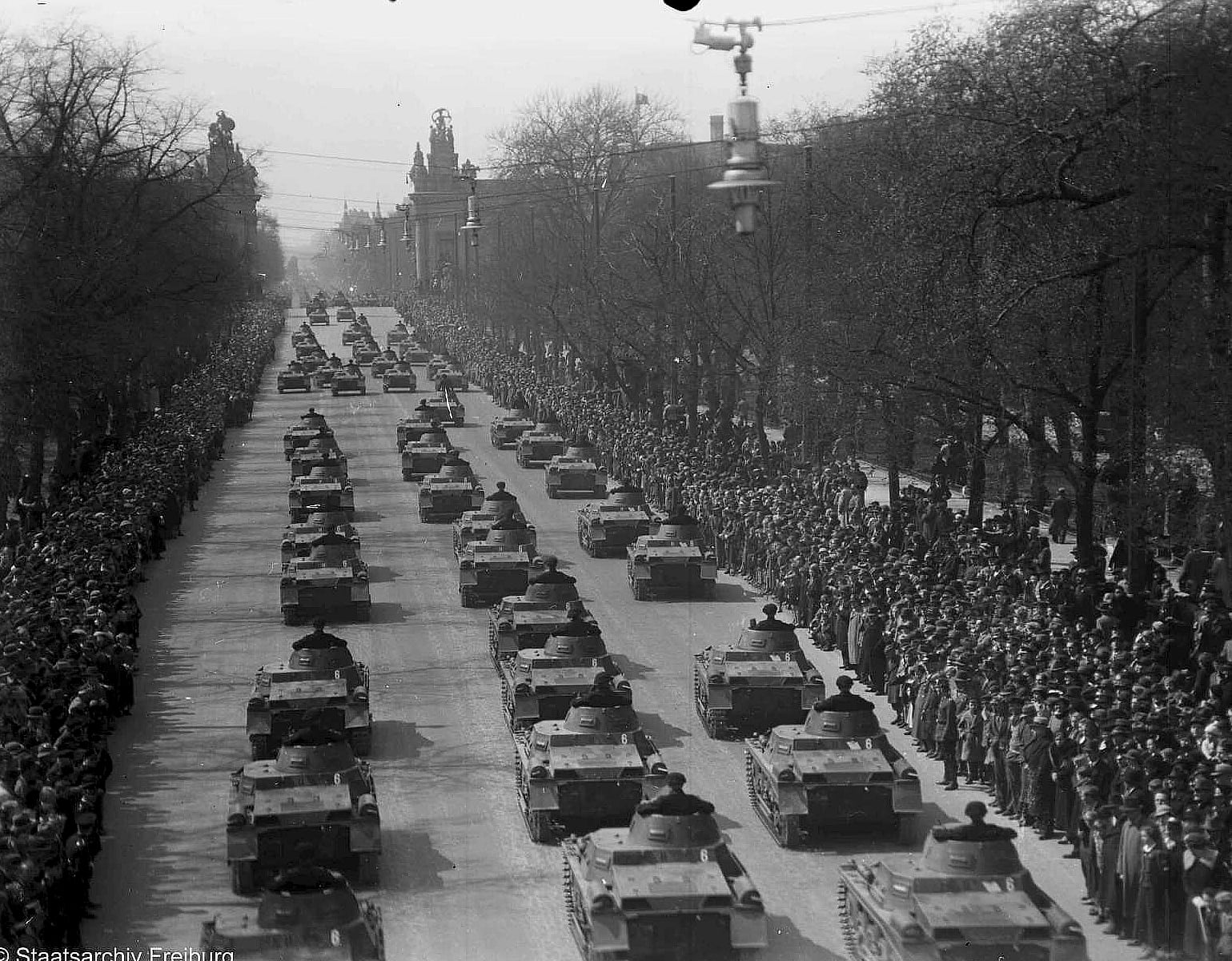 Columns of tanks parading along a broad tree-lined Berlin avenue between two walls of spectators