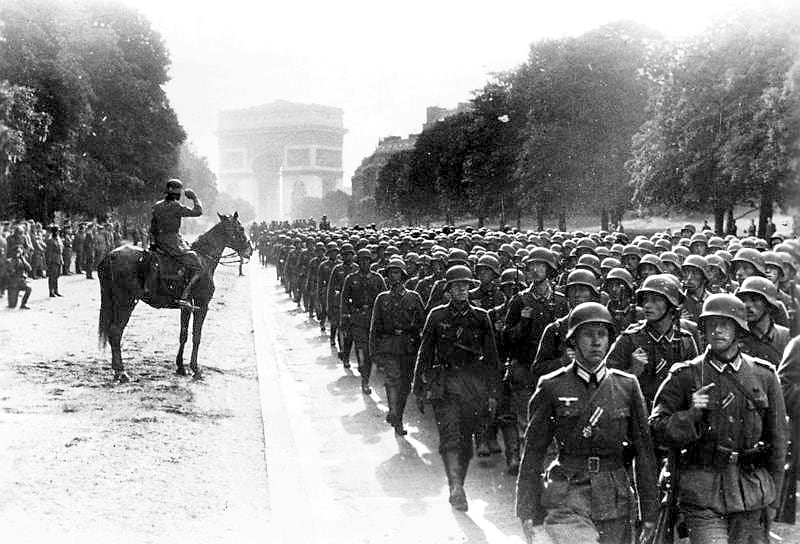 German soldiers marching along the Avenue Foch in Paris, with the Arc de Triomphe in the background and a mounted officer saluting