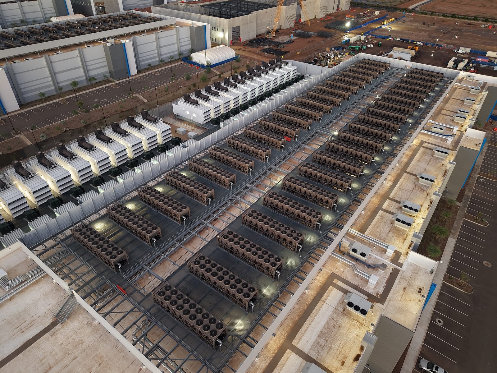 Aerial view of the roof of a large data centre covered in rows of cooling units with dozens of fans, next to a row of generators